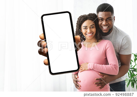 Cheerful african american expecting showing smartphone with empty screen Cheerful african american expecting showing smartphone with empty screen 92498887
