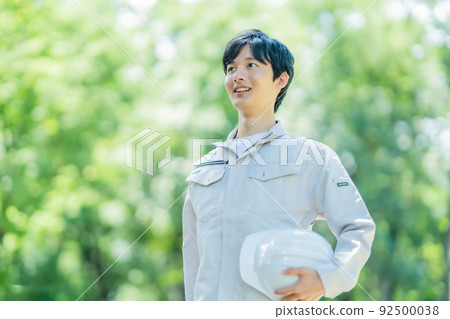 一位工程師帶著頭盔在新鮮的綠色前行走 一位工程師帶著頭盔在新鮮的綠色前行走 92500038