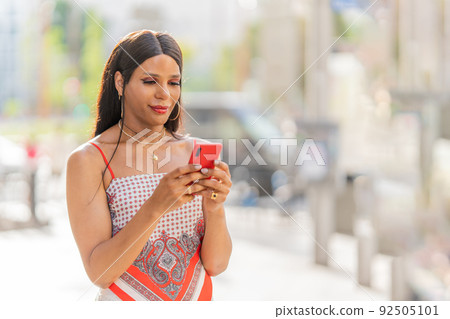 Transgender woman using the mobile outdoors. Mid shot Transgender woman using the mobile outdoors. Mid shot 92505101
