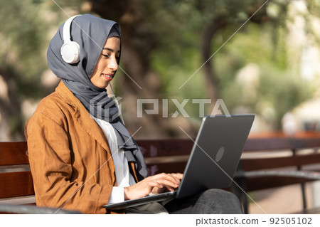 Muslim woman using a laptop while sitting on a park 92505102
