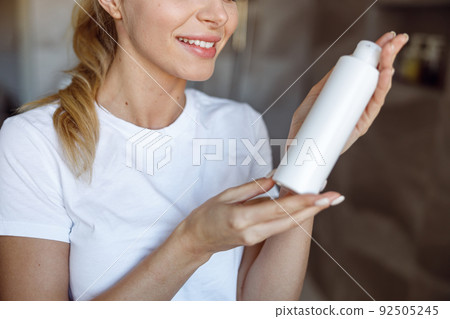 Skin care product in hands of cheerful Caucasian woman. Close up. Body lotion. 92505245