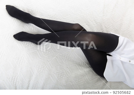 Beautiful long female legs in stockings. Girl putting on stockings at home in a white room sitting on the bed. Black tights. Varicose veins prevention. Woman body in underwear. Beautiful long female legs in stockings. Girl putting on stockings at home in a white room sitting on the bed. Black tights. Varicose veins prevention. Woman body in underwear. 92505682