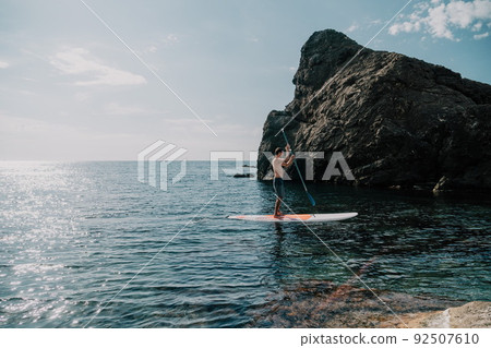 Side view foto of a man swiming and relaxing on the sup board. Sportive man in the sea on the Stand Up Paddle Board SUP. The concept of an active and healthy life in harmony with nature. 92507610