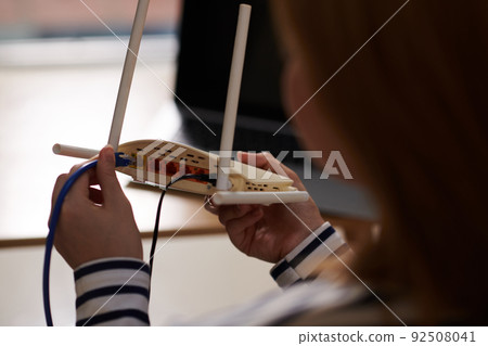 Woman Plugging Cord in Wi-Fi Couter 92508041