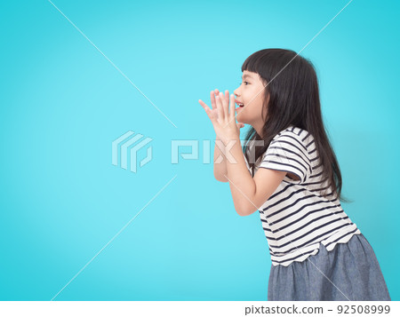 Cute little girl holding hands near mouth and making announcement, screaming on blue background with copy space. 92508999