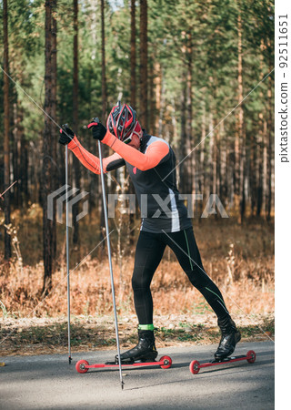 Training an athlete on the roller skaters. Biathlon ride on the roller skis with ski poles, in the helmet. Autumn workout. Roller sport. The athlete does the workout. Training an athlete on the roller skaters. Biathlon ride on the roller skis with ski poles, in the helmet. Autumn workout. Roller sport. The athlete does the workout. 92511651