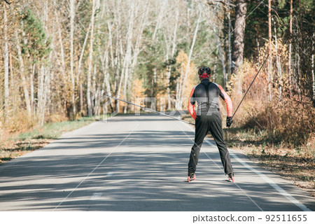 Training an athlete on the roller skaters. Biathlon ride on the roller skis with ski poles, in the helmet. Autumn workout. Roller sport. Training an athlete on the roller skaters. Biathlon ride on the roller skis with ski poles, in the helmet. Autumn workout. Roller sport. 92511655