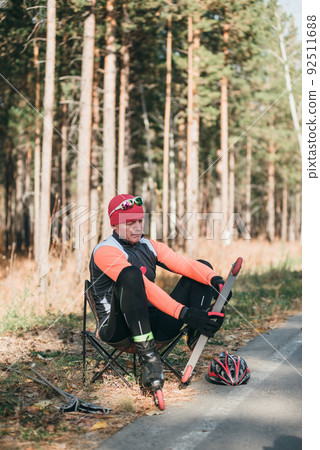 Training an athlete on the roller skaters. Biathlon ride on the roller skis with ski poles, in the helmet. Athlete is getting ready to start. Autumn workout. Roller sport. 92511688
