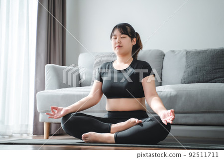 Asian chubby woman sitting on the floor in living room practice yoga lesson. female having meditate training class.. Asian chubby woman sitting on the floor in living room practice yoga lesson. female having meditate training class.. 92511711