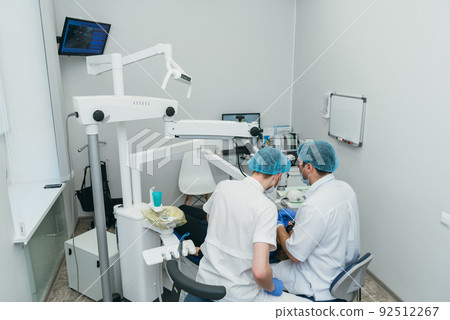 Doctor used microscope. Dentist is treating patient in modern dental office. Operation is carried out using cofferdam. Client is inserted and restored teeth, make denture. 92512267