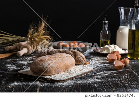 Beautiful still life with different kinds of bread, grain, flour on weight, ears of wheat, pitcher of milk and eggs 92514743