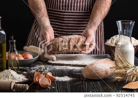 Chef holds the fresh bread in hand. Man preparing dough at table in kitchen. Chef holds the fresh bread in hand. Man preparing dough at table in kitchen. 92514745