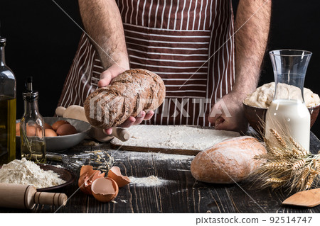 Chef holds the fresh bread in hand. Man preparing dough at table in kitchen. Chef holds the fresh bread in hand. Man preparing dough at table in kitchen. 92514747