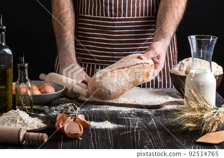 Chef holds the fresh bread in hand. Man preparing dough at table in kitchen. 92514765