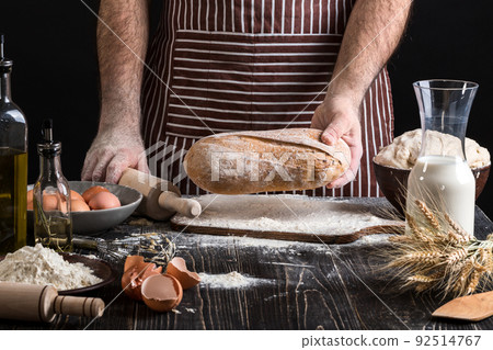Chef holds the fresh bread in hand. Man preparing dough at table in kitchen. 92514767