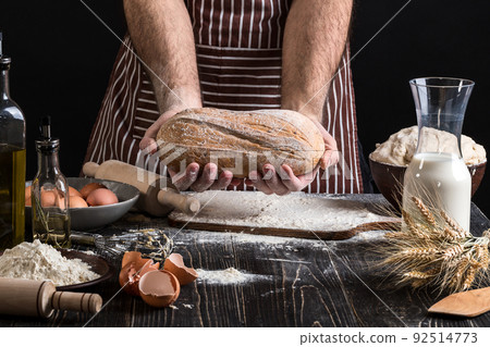 Chef holds the fresh bread in hand. Man preparing dough at table in kitchen. Chef holds the fresh bread in hand. Man preparing dough at table in kitchen. 92514773