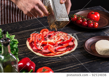 Cook in the kitchen putting the ingredients on the pizza. Pizza concept. Production and delivery of food. Cook in the kitchen putting the ingredients on the pizza. Pizza concept. Production and delivery of food. 92514836