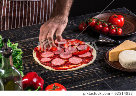Cook in the kitchen putting the ingredients on the pizza. Pizza concept. Production and delivery of food. 92514852