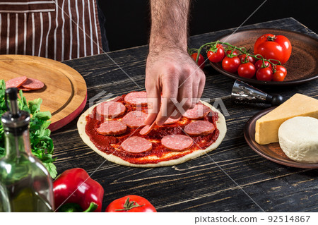 Cook in the kitchen putting the ingredients on the pizza. Pizza concept. Production and delivery of food. Cook in the kitchen putting the ingredients on the pizza. Pizza concept. Production and delivery of food. 92514867