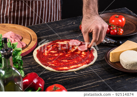 Cook in the kitchen putting the ingredients on the pizza. Pizza concept. Production and delivery of food. 92514874