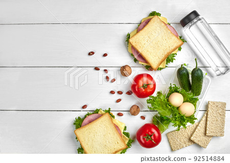 Healthy lunch box with sandwiches, eggs and fresh vegetables, bottle of water and nuts on rustic wooden background. Top view with copy space Healthy lunch box with sandwiches, eggs and fresh vegetables, bottle of water and nuts on rustic wooden background. Top view with copy space 92514884