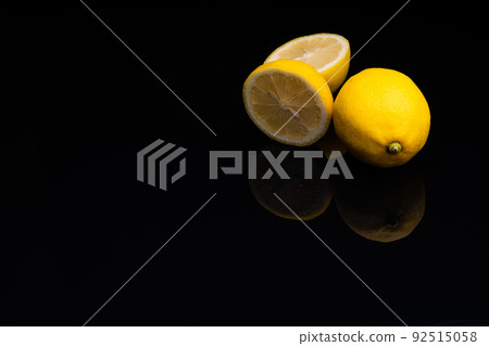 A photo of a lemon with a visible cross section taken against a black reflective background 92515058