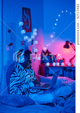 African teenager spending his leisure time for playing online games on laptop in his room at night 92515482
