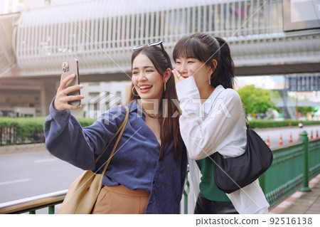 Happy two young women make selfie video call with her friend on city street. Happy two young women make selfie video call with her friend on city street. 92516138