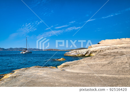 Unique white rocks of Sarakiniko beach, Aegean sea, Milos island , Greece. No people, lonely sailboat, empty cliffs, summer sunshine, clear sea waters 92516420