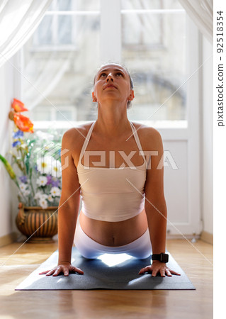 Young woman in white sportswear stretching her spine in upward dog yoga pose 92518354