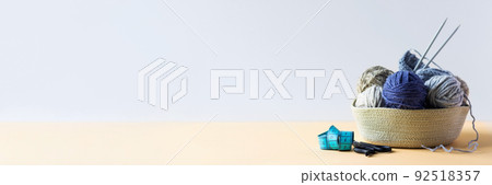 Gray and blue balls of thread in a beige basket with knitting needles for knitting warm clothes with scissors and a centimeter, knitting banner Gray and blue balls of thread in a beige basket with knitting needles for knitting warm clothes with scissors and a centimeter, knitting banner 92518357