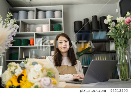 Portrait of beautiful female florist in apron working on laptop in flower store. 92518393