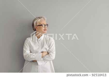 Portrait of confident mature businesswoman in shirt and glasses standing by grey copy space wall 92518413