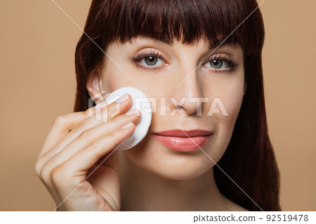 Beautiful red-haired woman, girl cleanses her skin with a cotton pad. 92519478