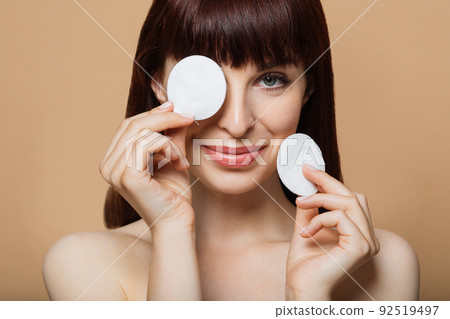 Joyful young female covering eye with cotton pad 92519497