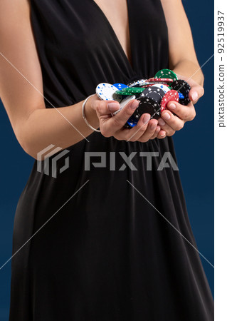 Elegant female casino player holding a handful of chips on dark blue background, hands close up Elegant female casino player holding a handful of chips on dark blue background, hands close up 92519937