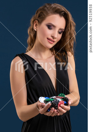 Elegant female casino player holding a handful of chips on dark blue background Elegant female casino player holding a handful of chips on dark blue background 92519938