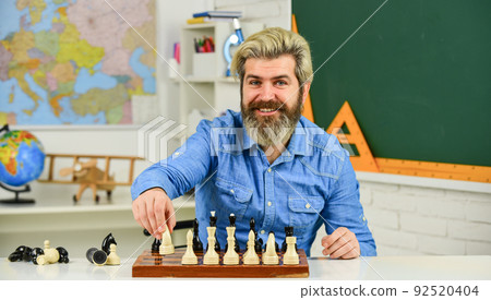 pieces and boards. happy school teacher. thinking of attacking and capturing opponent chess pieces. thinking of next move. bearded man training for chess competition. chess figures on wooden board pieces and boards. happy school teacher. thinking of attacking and capturing opponent chess pieces. thinking of next move. bearded man training for chess competition. chess figures on wooden board 92520404
