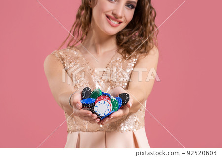 Young beautiful emotional woman with chips in hands on a pink background in the studio. Poker 92520603
