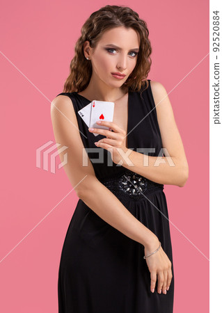 Young woman holding two aces in hand against on pink background Young woman holding two aces in hand against on pink background 92520884