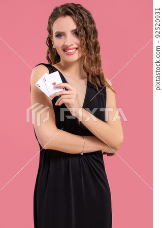 Young woman holding two aces in hand against on pink background Young woman holding two aces in hand against on pink background 92520931