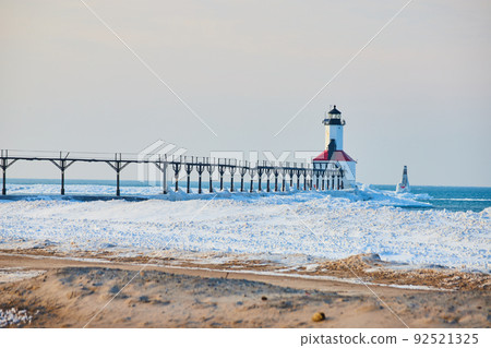 Beach covered in ice with walkway leading to red and white lighthouse Beach covered in ice with walkway leading to red and white lighthouse 92521325