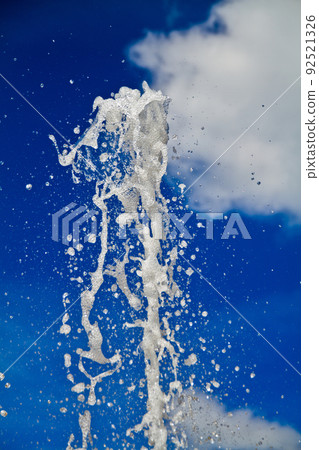 Water fountain spouts upwards on a blue sky with clouds 92521326