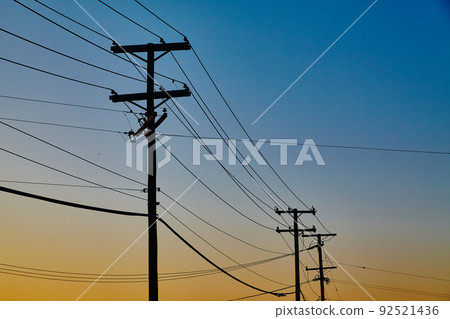 Power lines extend into the distance, silhouetted by the orange setting sun Power lines extend into the distance, silhouetted by the orange setting sun 92521436