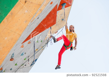 Sportsman climber moving up on steep rock, climbing on artificial wall. 92521508