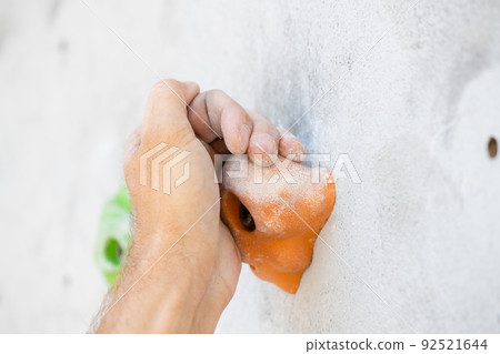 Close-up of a male hand with magnesium powder grabbing a hold of climbing wall. 92521644