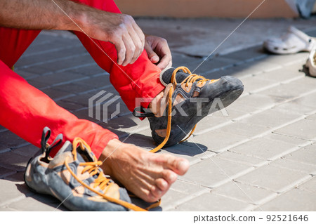A man puts on climbing shoes while sitting at a climbing wall. A man puts on climbing shoes while sitting at a climbing wall. 92521646