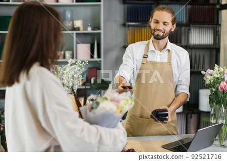 Attractive young man receives payment for a bouquet of flowers with credit card in flower shop Attractive young man receives payment for a bouquet of flowers with credit card in flower shop 92521716