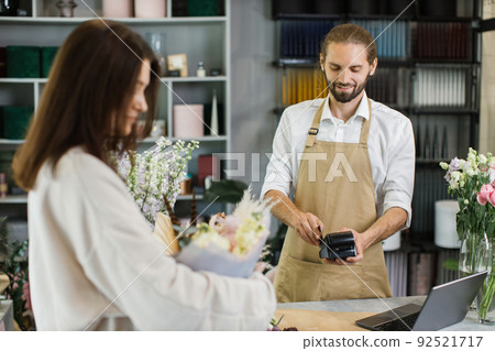 Attractive young man receives payment for a bouquet of flowers with credit card in flower shop Attractive young man receives payment for a bouquet of flowers with credit card in flower shop 92521717