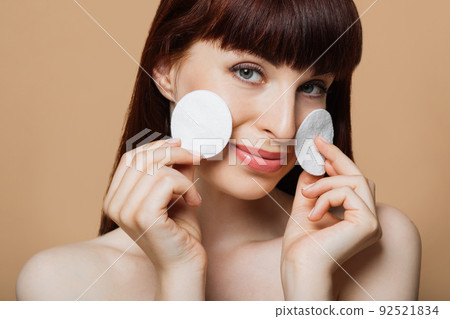 woman holding white cosmetic sponges and smiling on camera over beige background. 92521834
